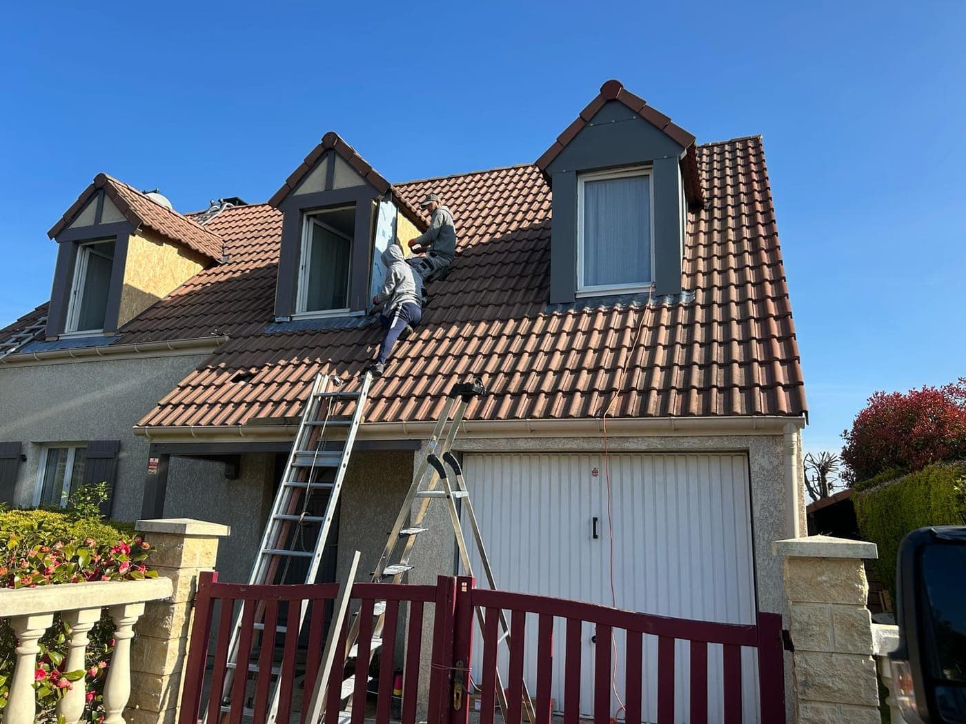 Couvreur au travail sur la toiture en tuile d'une maison à lucarnes