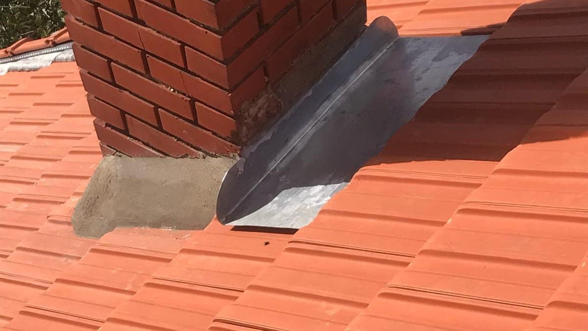 Pièce de zinc façonnée au raccord entre une souche en brique et la couverture